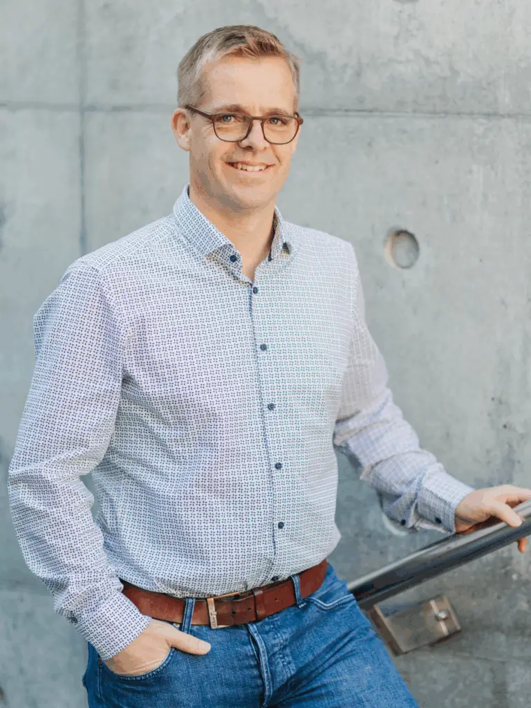 Mann mit Brille in Hemd lehnt an Wand